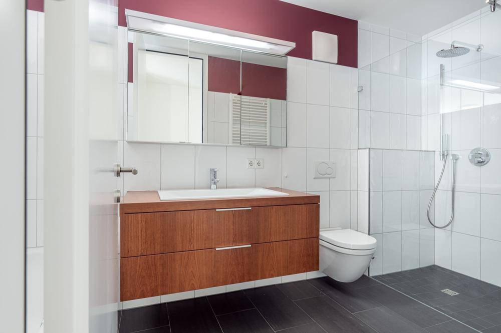 Modernes Badezimmer mit ebenerdiger Dusche, Holzwaschtisch und Wand-WC.