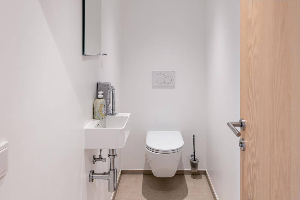 Praktisches Gäste-WC mit kleinem Waschbecken und wandhängender Toilette in schlichtem Design.