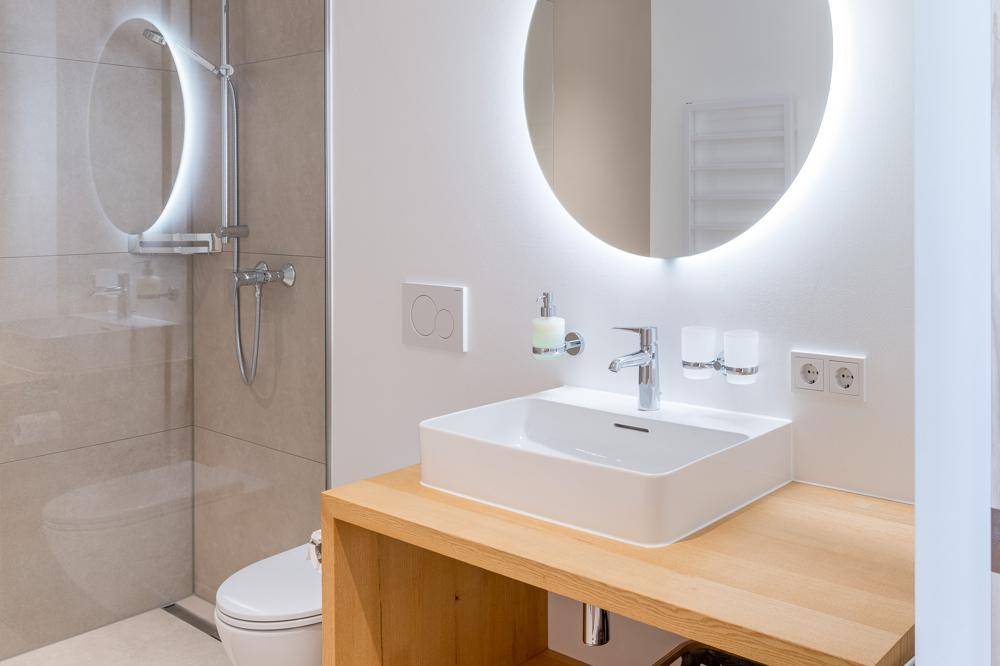 Elegantes Badezimmer mit beleuchtetem Spiegel, modernem Waschbecken und wandhängendem WC.