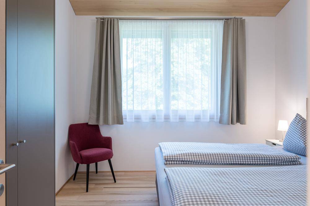 Gemütliches Schlafzimmer mit zwei Einzelbetten, Holzboden und einem großen Fenster.