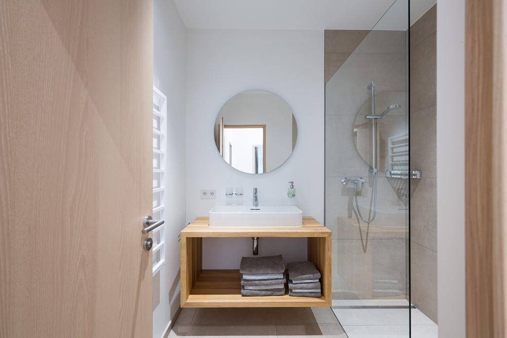 Modernes Badezimmer mit Holzwaschtisch, rundem Spiegel und einer geräumigen begehbaren Dusche.