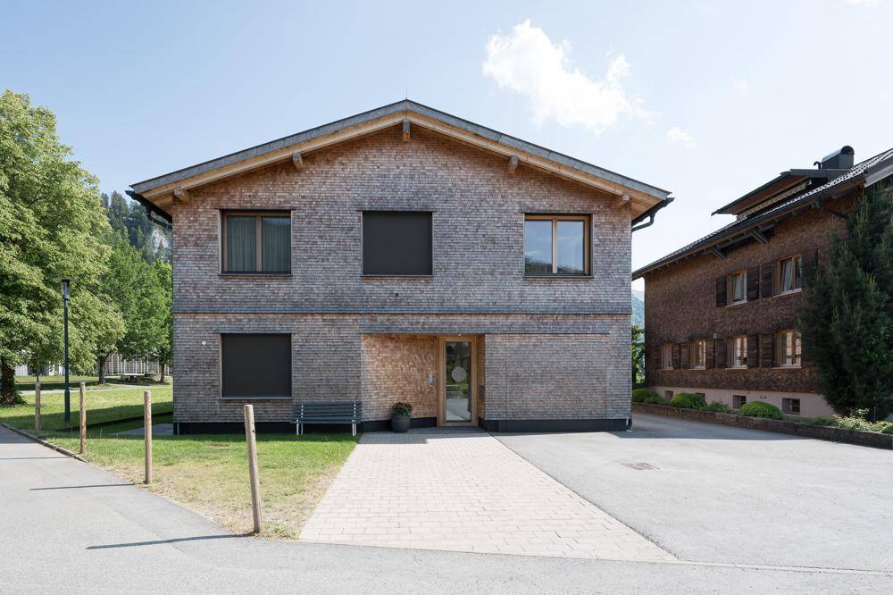 Vorderansicht des modernen Hauses mit Holzschindelfassade, Eingangsbereich und gepflasterter Zufahrt.