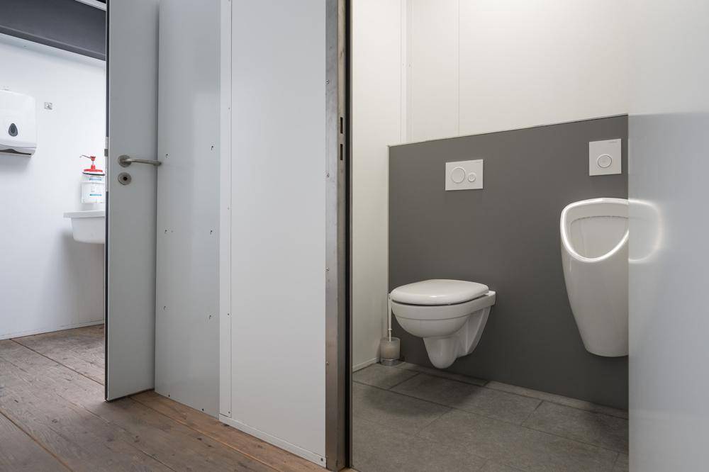 Separate Toilette mit wandhängendem WC und Urinal, in schlichtem Design gehalten.