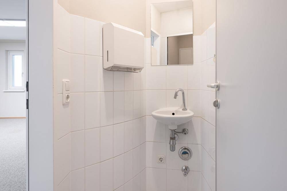 Kleine Gästetoilette mit Waschbecken, Spiegel und weißen Fliesen an den Wänden.