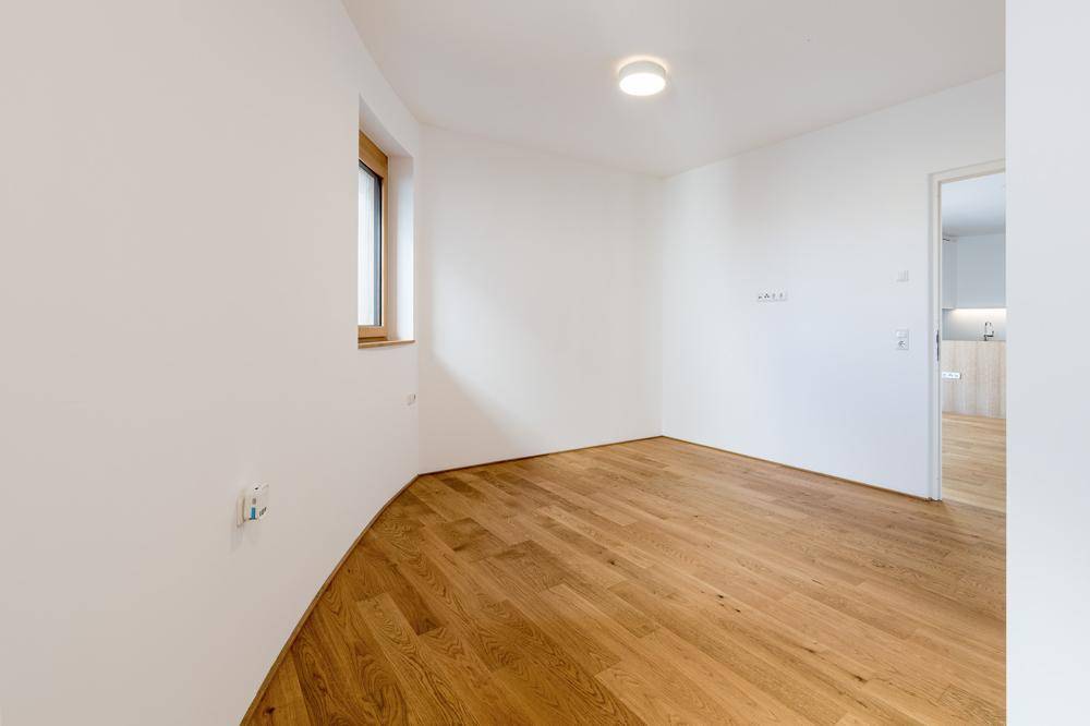 Helles Zimmer mit Holzboden und einem Fenster, ideal als Schlaf- oder Arbeitszimmer.