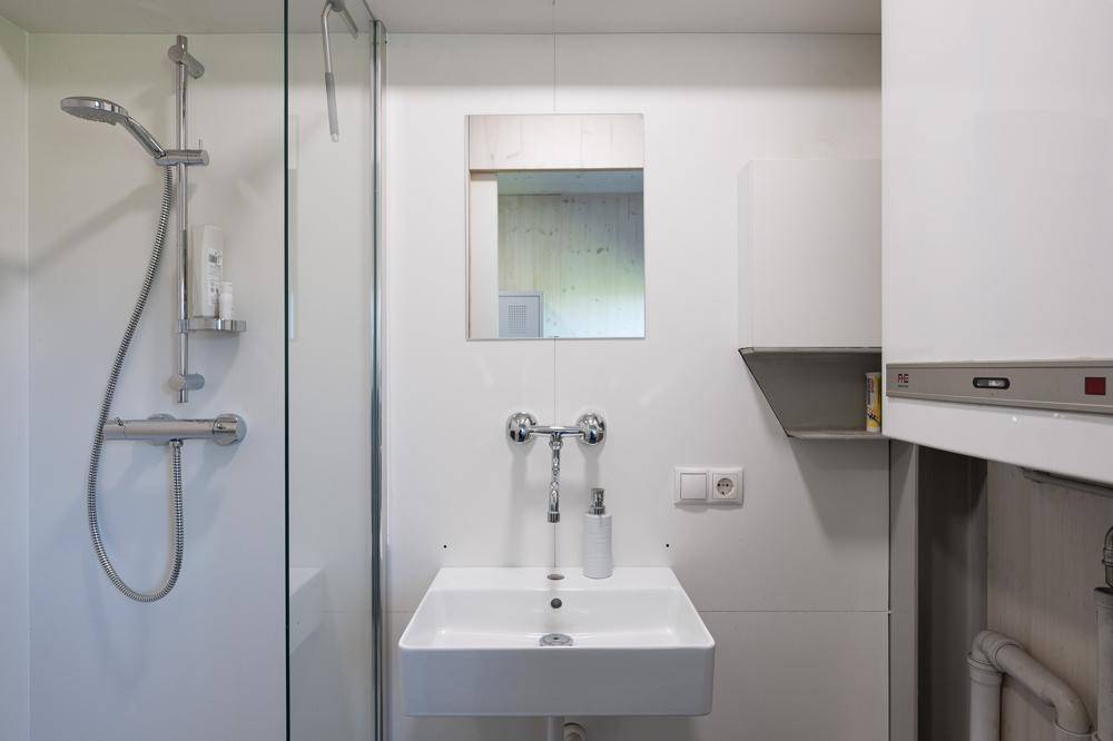Modernes Badezimmer mit Duschkabine, Waschbecken und Spiegel in schlichtem Weiß.