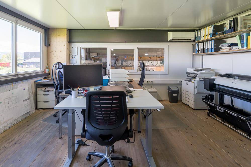 Helles und funktionales Büro mit mehreren Arbeitsplätzen, Regalen und Blick ins Grüne.