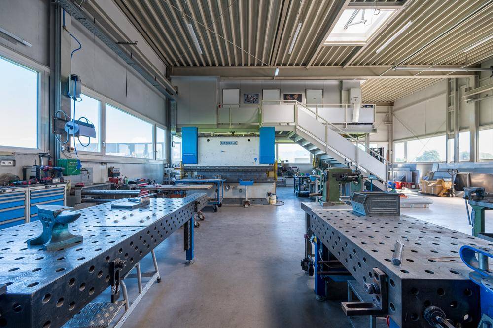 Moderne Werkstatt mit Präzisionsmaschinen, großen Arbeitsflächen und einer Treppe zu einem oberen Bereich.
