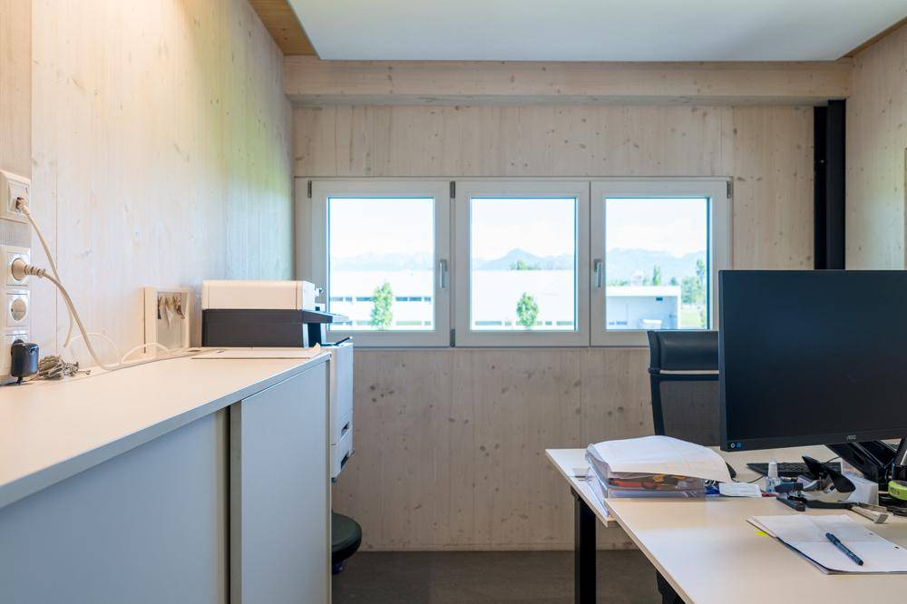 Büro mit Holzwänden, einem Schreibtisch und einem weiten Blick auf den See und die Berge.