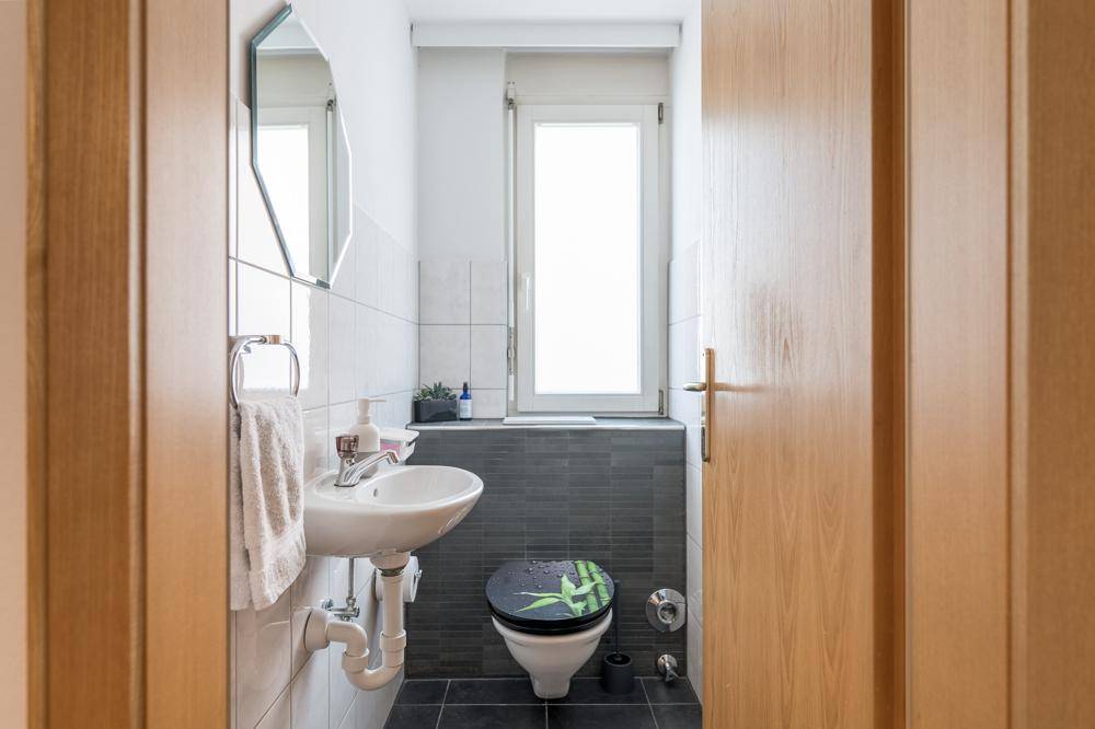 Kleines Gäste-WC mit Fenster, Waschbecken und dunklen Bodenfliesen.