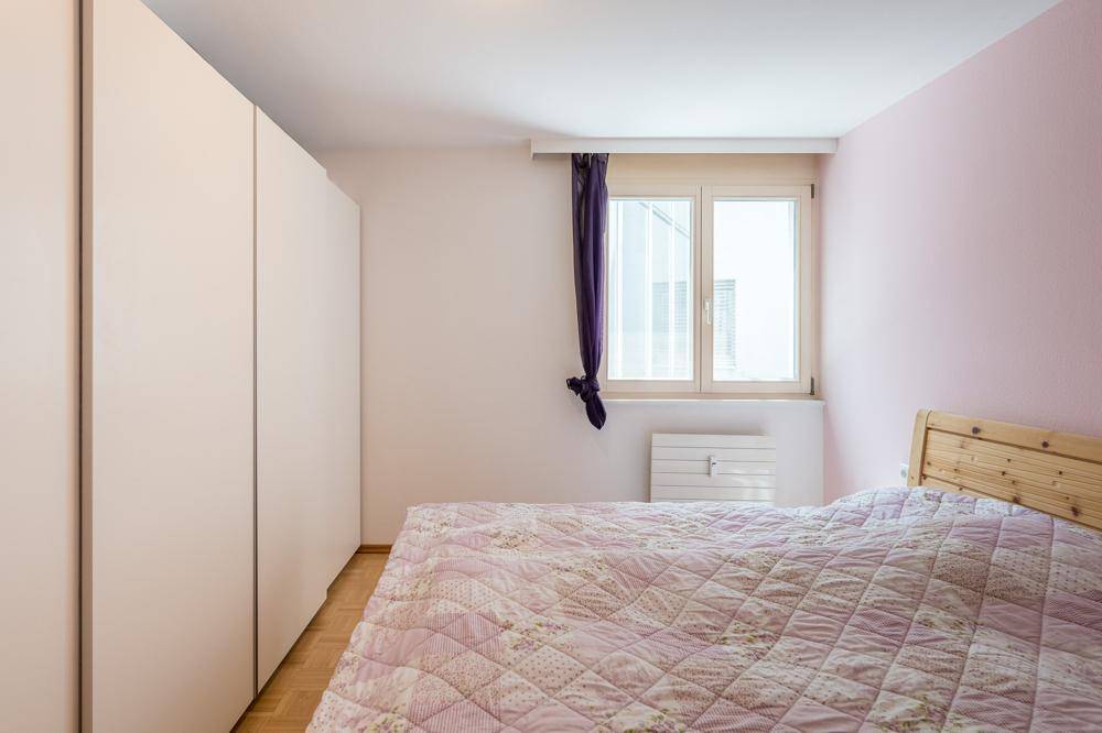 Schlafzimmer mit hellem Parkettboden, Einbauschrank und Fenster.