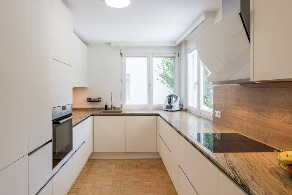Moderne Küche mit weißen Schränken, Holz-Arbeitsplatten und Induktionskochfeld.