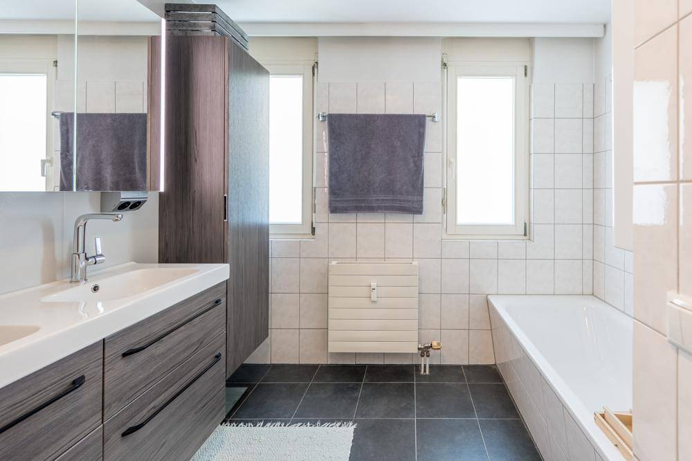 Modernes Badezimmer mit Badewanne, Doppelwaschbecken und großen Fliesen.