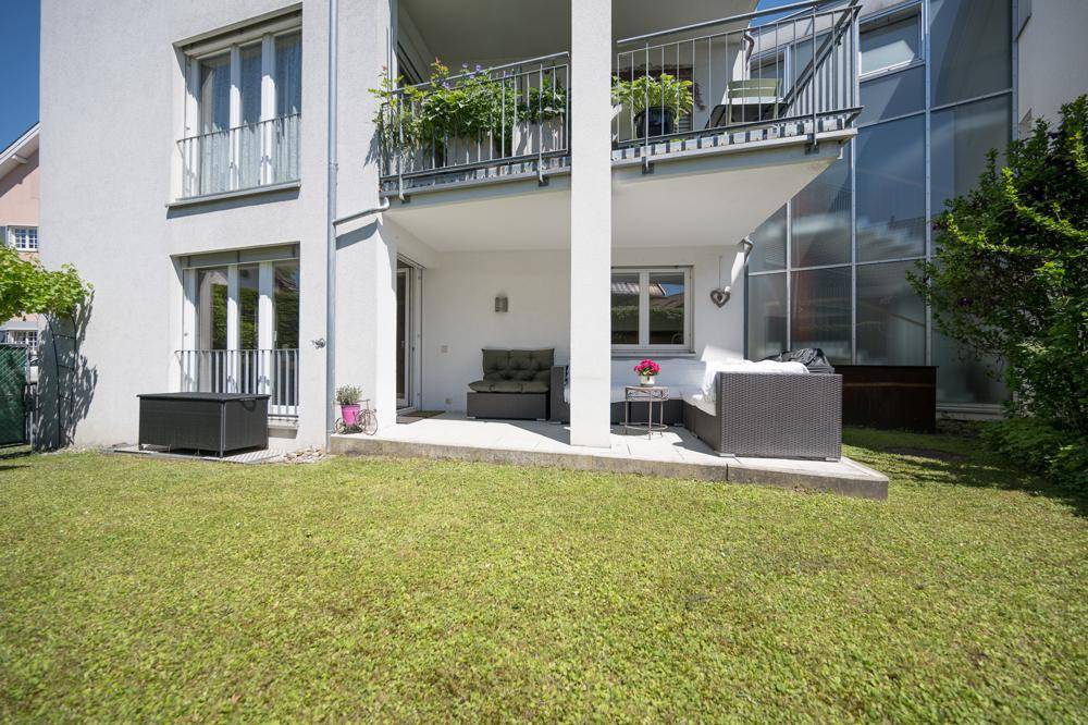 Sonniger Gartenbereich mit Rasenfläche und einer überdachten Terrasse mit Sitzgelegenheiten.