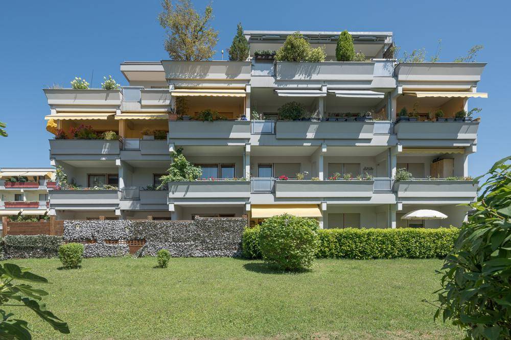 Modernes Mehrfamilienhaus mit zahlreichen Balkonen, Markisen und gepflegter Grünfläche.