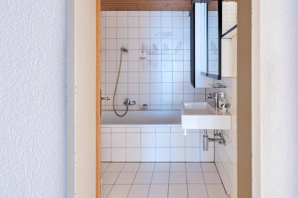 Gefliestes Badezimmer mit Badewanne, Duschfunktion, Waschbecken und Holzdecke.