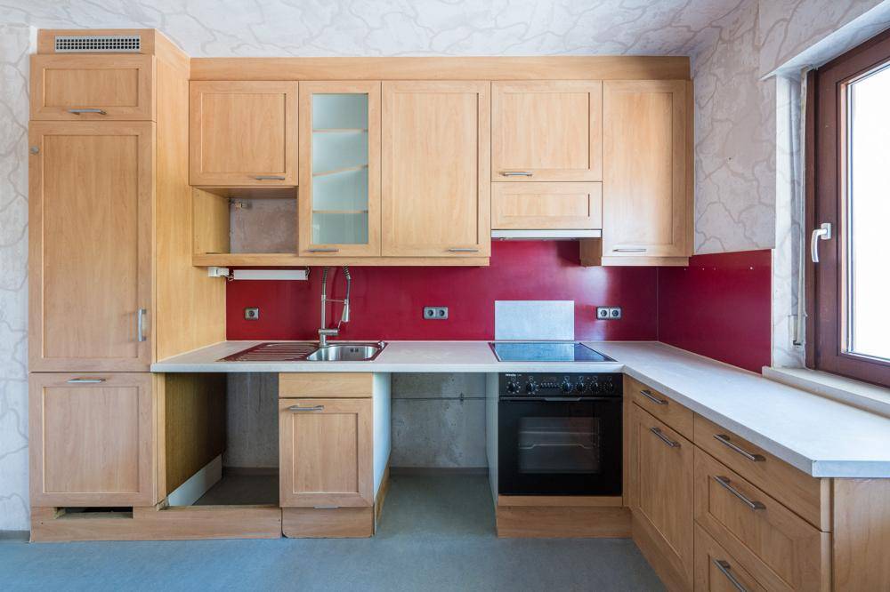 Funktionale Küche mit hellen Holzschränken, roter Rückwand und Fenster für Tageslicht.