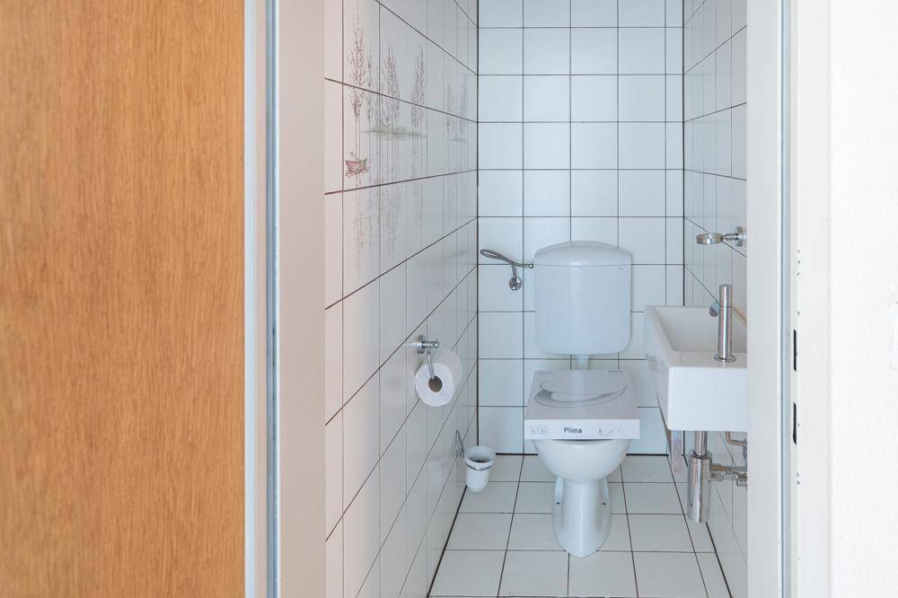 Kleines Gäste-WC mit weißen Fliesen, Toilette und Handwaschbecken, sehr gepflegt.