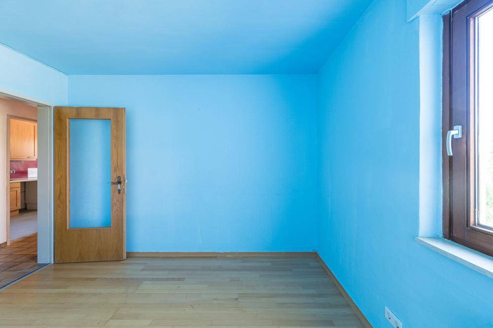 Heller Raum mit leuchtend blauen Wänden, Laminatboden und Zugang zur Küche.