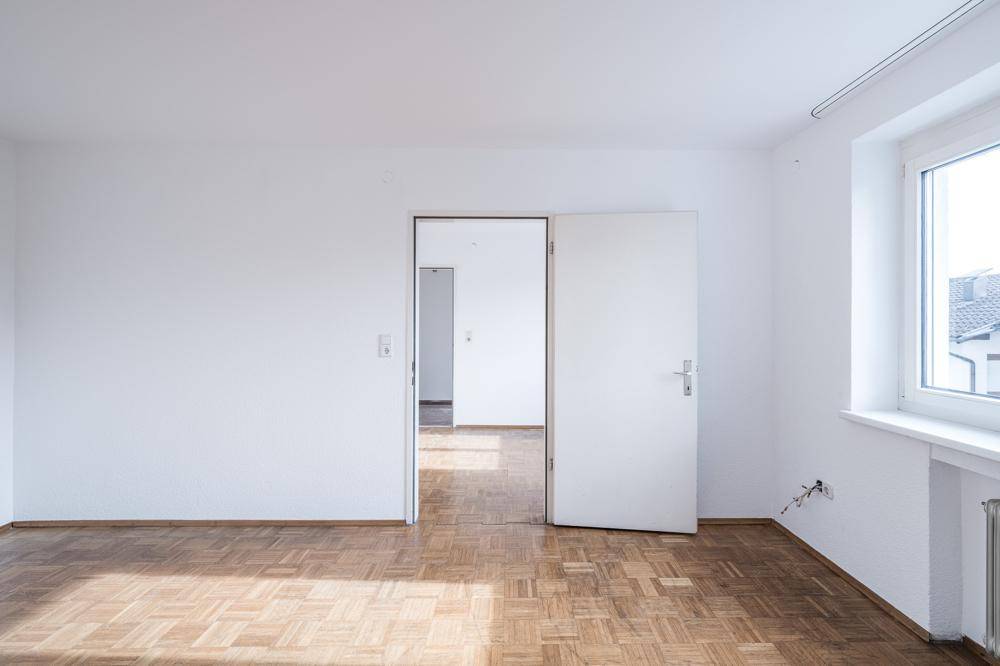 Heller Raum mit Parkettboden und Zugang zu einem weiteren Zimmer, ideal für flexible Nutzung.