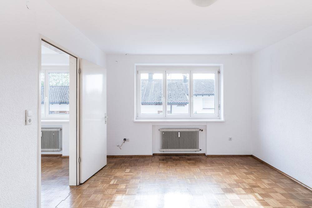 Geräumiger, heller Raum mit Parkettboden und großem Fenster, ideal als Wohnzimmer.
