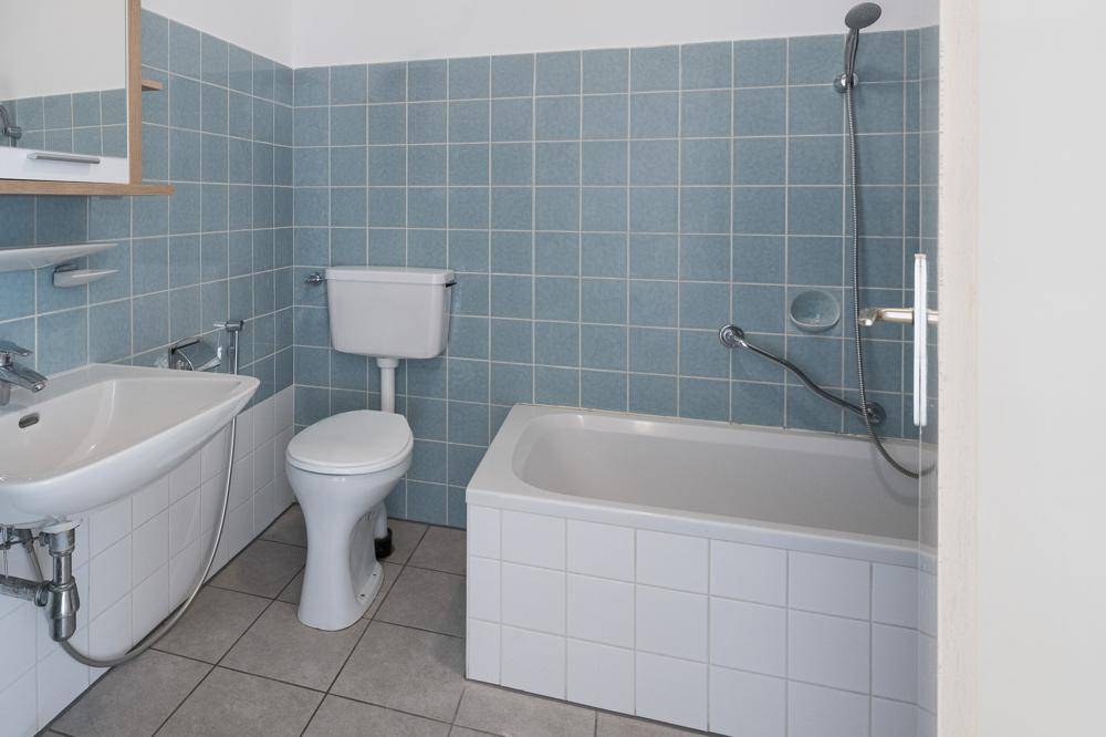 Badezimmer mit blauen Fliesen, Badewanne und Waschbecken in Standardausstattung.