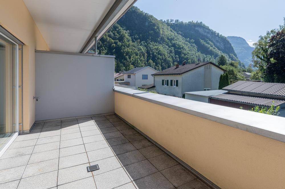 Geräumiger Balkon mit Fliesenboden und weitem Blick auf grüne Berge und Häuser.