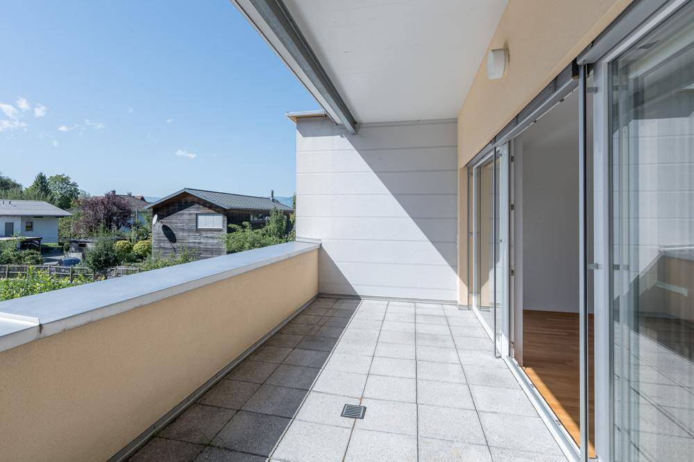 Sonniger Balkon mit Fliesenboden und Blick auf die umliegende Wohngegend und Gärten.