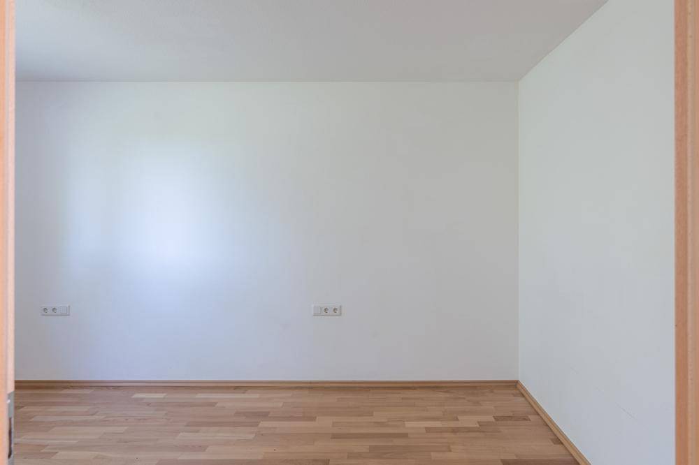 Leeres Zimmer mit hellem Parkettboden und weißen Wänden, bereit zur individuellen Gestaltung.