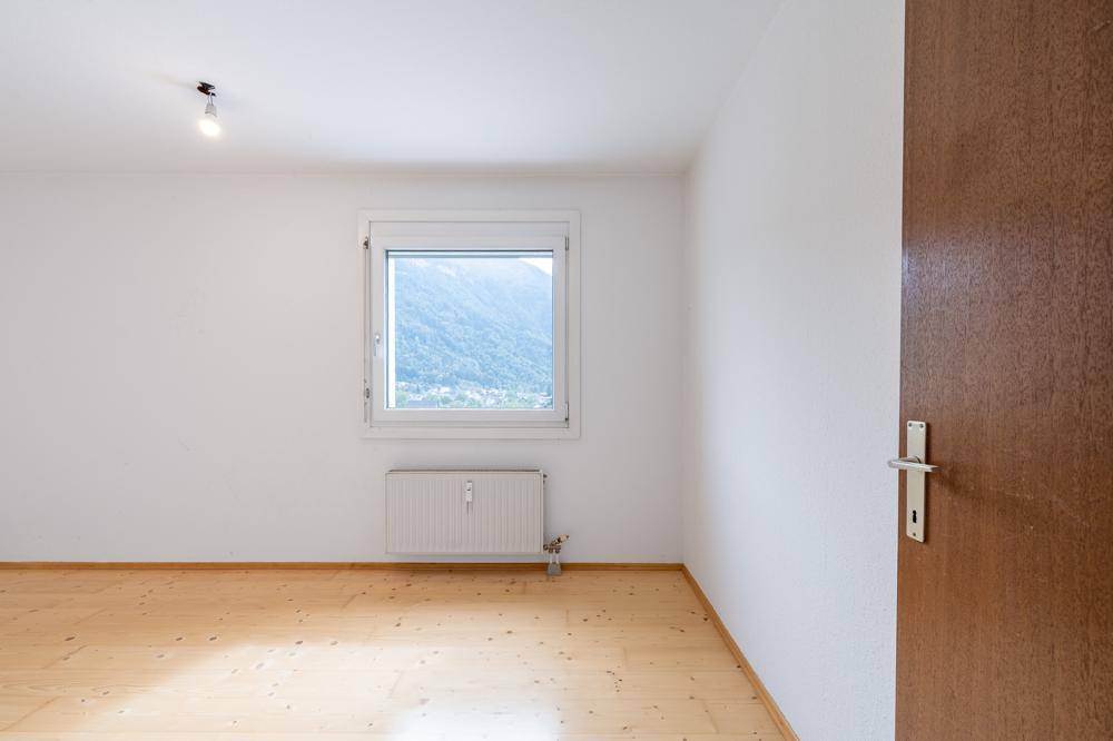 Leeres Schlafzimmer mit hellem Holzfußboden, weiß gestrichenen Wänden und Fenster mit Bergblick.
