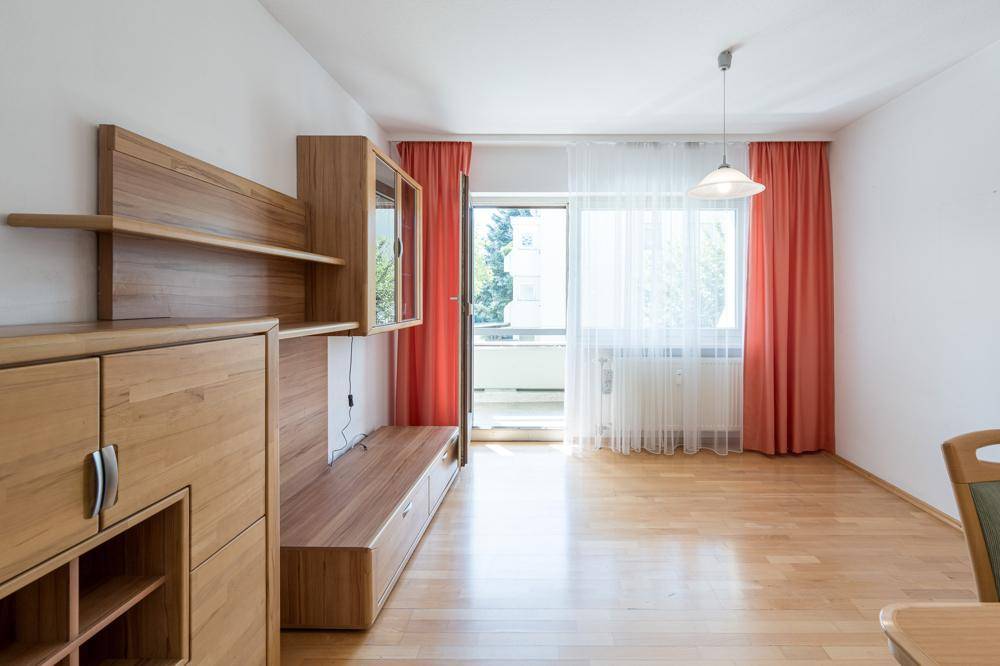 Helles Wohnzimmer mit Holzmöbeln, Parkettboden und Zugang zu einem Balkon.