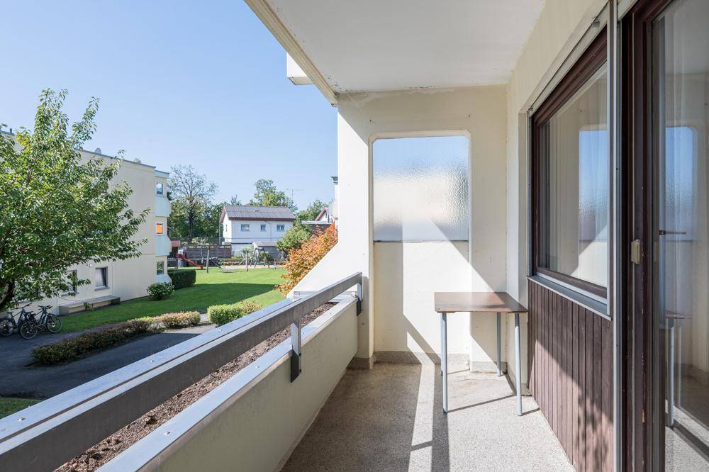 Sonniger Balkon mit Blick auf die grüne Umgebung und den Spielplatz.