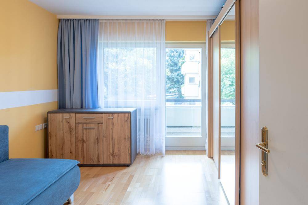 Helles Schlafzimmer mit gelben Wänden, Parkettboden und großem Fenster.