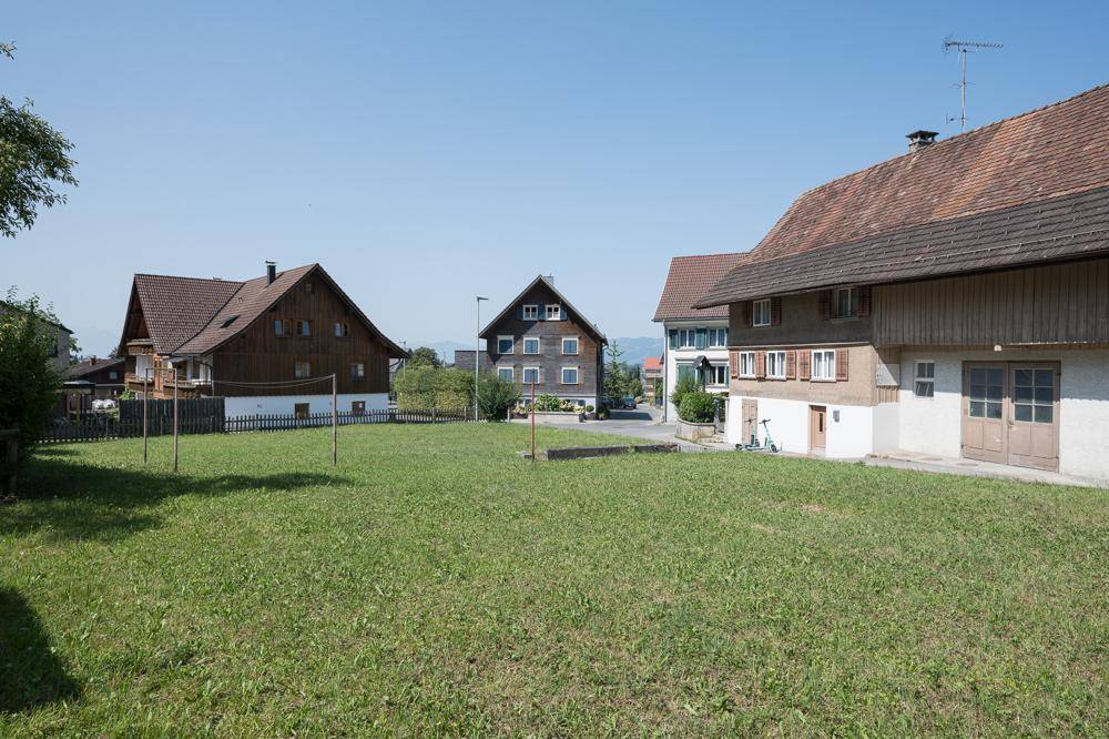 Weitläufige Rasenfläche eines Grundstücks mit Blick auf benachbarte Gebäude und die Landschaft.
