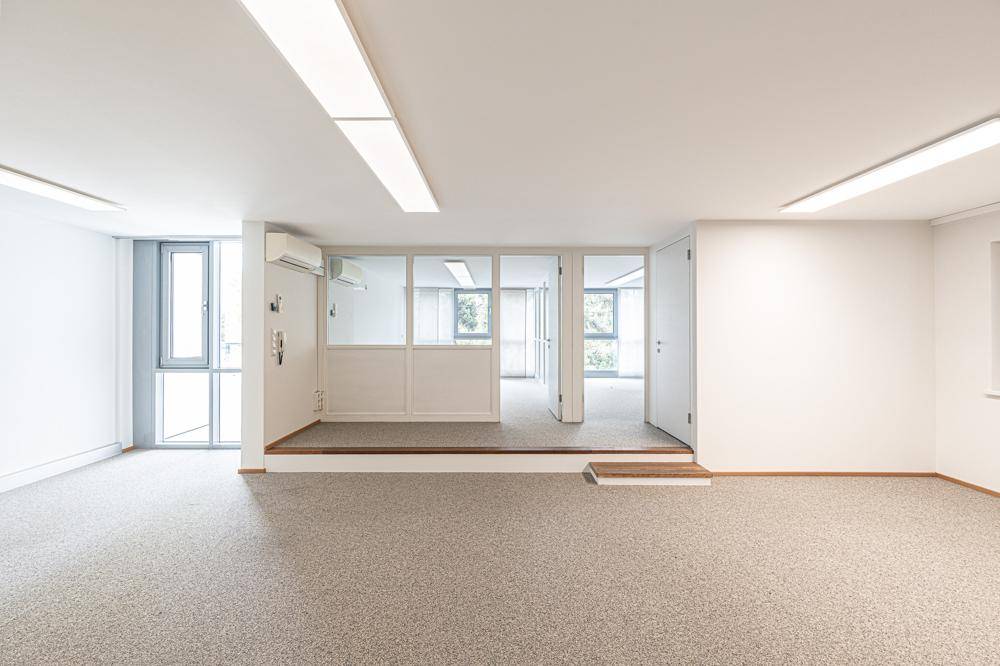 Großzügiger Bürobereich mit Teppichboden, Klimaanlage und Fenstern, die viel Tageslicht hereinlassen.