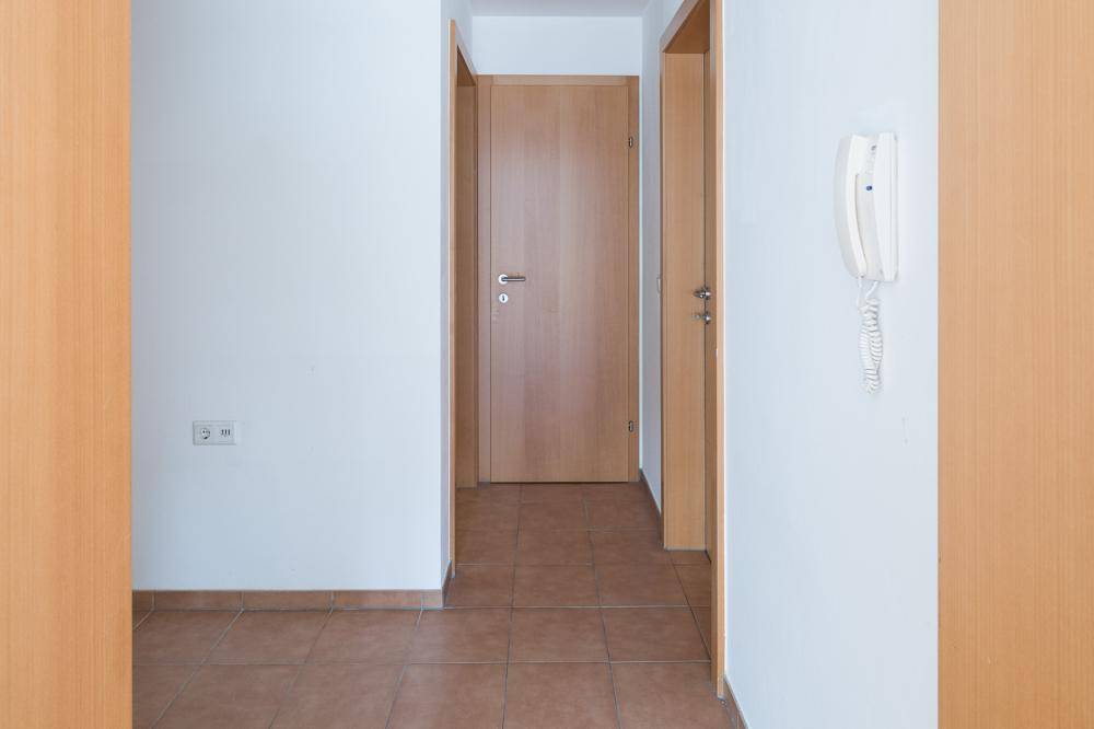 Heller Flur mit Fliesenboden, Holztüren und einer Gegensprechanlage an der Wand.