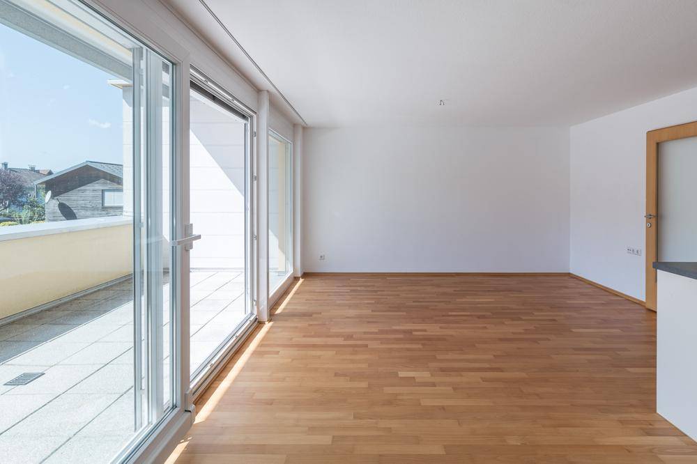 Heller Wohnbereich mit Holzboden und großen Schiebetüren, die auf einen sonnigen Balkon führen.