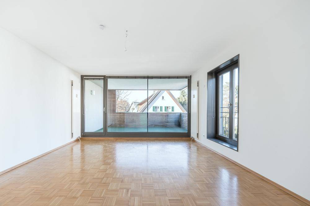Helles, leeres Zimmer mit Parkettboden und Zugang zu einem Balkon, ideal als Wohnbereich.