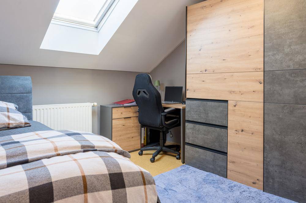 Jugendzimmer mit Schreibtisch, Kleiderschrank und Dachfenster für natürliches Licht.