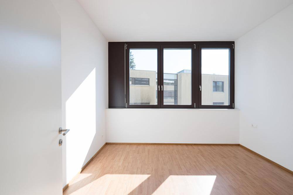 Lichtdurchfluteter, leerer Raum mit großen Fenstern und Laminatboden, bereit zur individuellen Gestaltung.