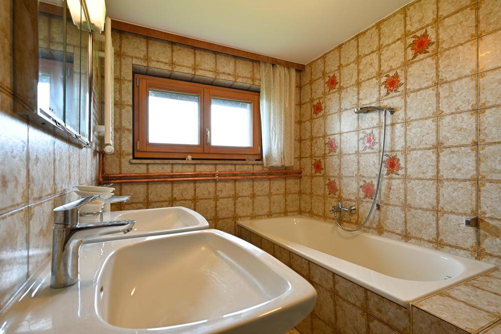 Badezimmer mit floral gemusterten Fliesen, Doppelwaschbecken, Badewanne und Fenster.