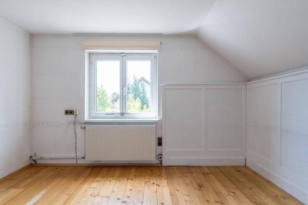 Helles Dachzimmer mit Holzfußboden, weißer Wandverkleidung und Fenster mit Ausblick.