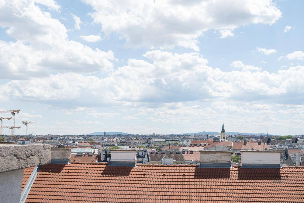Panoramablick über die Dächer der Stadt mit Bergen am Horizont unter blauem Himmel.