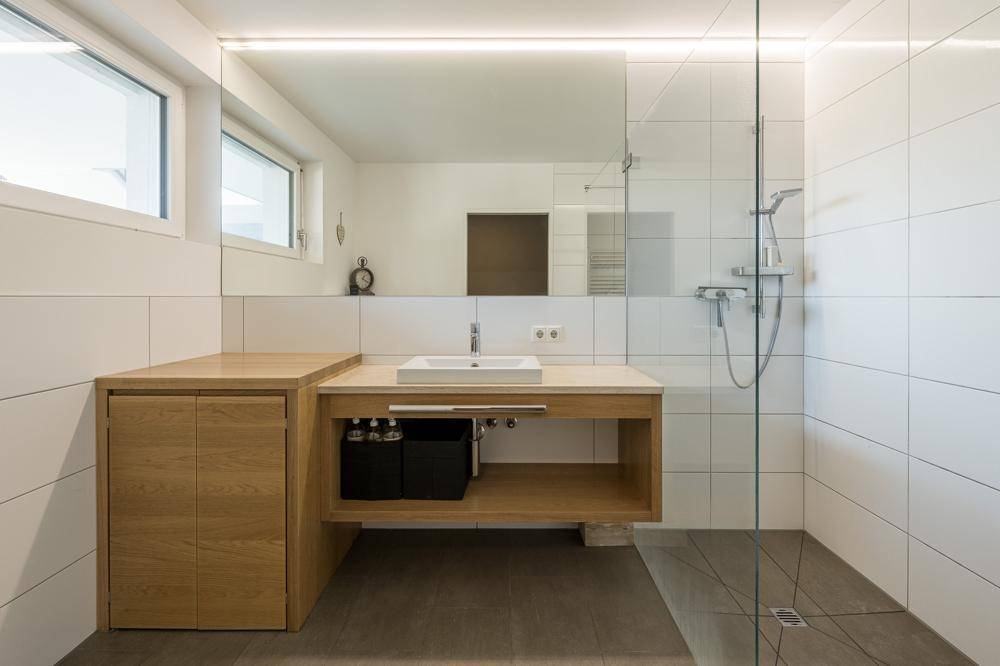 Modernes Badezimmer mit begehbarer Dusche, Holzwaschtisch und zwei Fenstern für viel Licht.