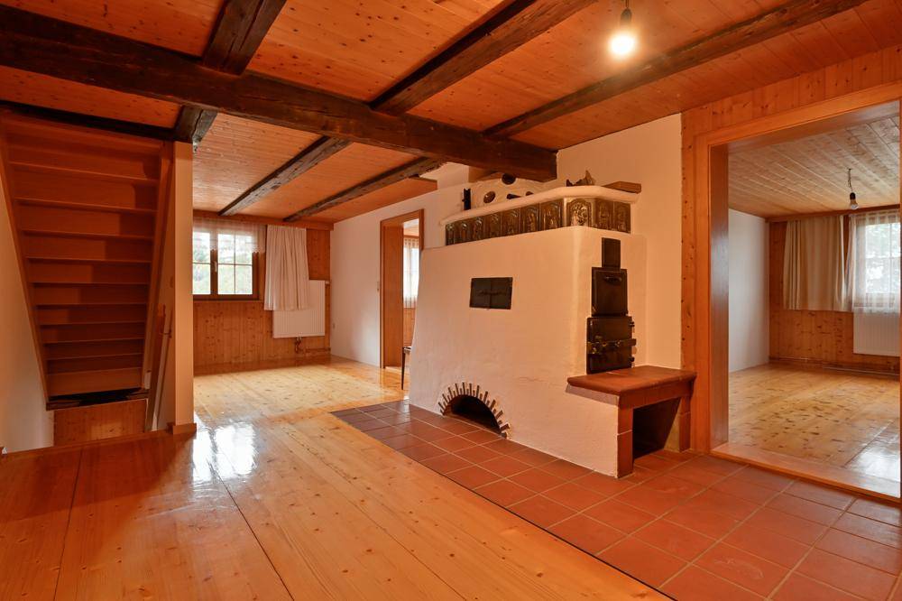 Offener Wohnbereich mit Holzbalken, Holzboden, Treppe und einem traditionellen Kachelofen.