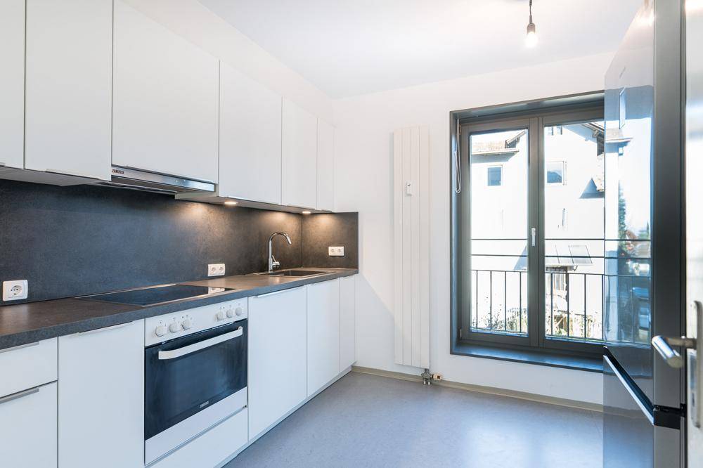 Moderne Einbauküche mit weißen Schränken, dunkler Arbeitsplatte und Fenster.