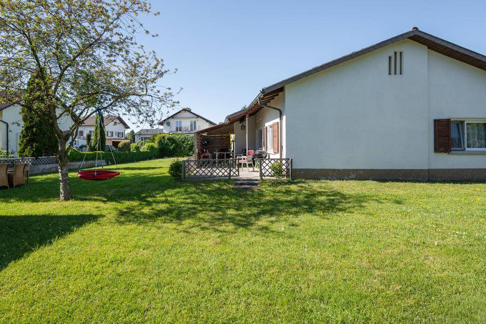 Sonniger Garten mit großer Rasenfläche, Schaukel und einer gemütlichen Terrasse am Haus.