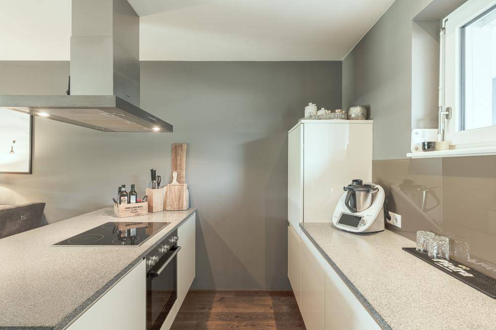 Moderne Einbauküche mit Induktionskochfeld, Dunstabzugshaube und Fenster für Tageslicht.