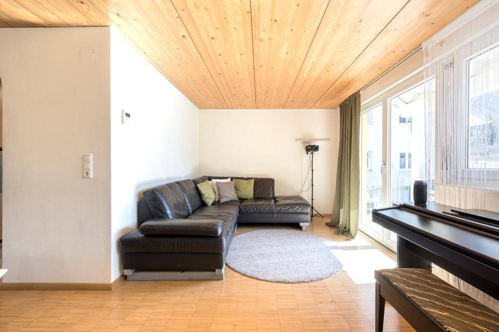Gemütliches Wohnzimmer mit Ledersofa, Holzbalkendecke und Zugang zum Balkon oder Garten.