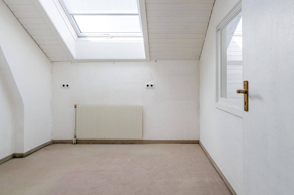 Heller Raum mit Dachfenstern, weiß gestrichenen Wänden und einem Heizkörper.